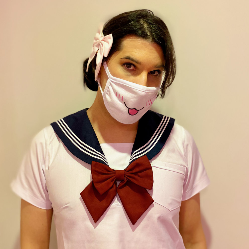 Rina looking at camera, wearing a Japanese schoolgirl uniform with stockings, a navy blue skirt, navy blue collar, red bow, and a big pink bow in her hair.