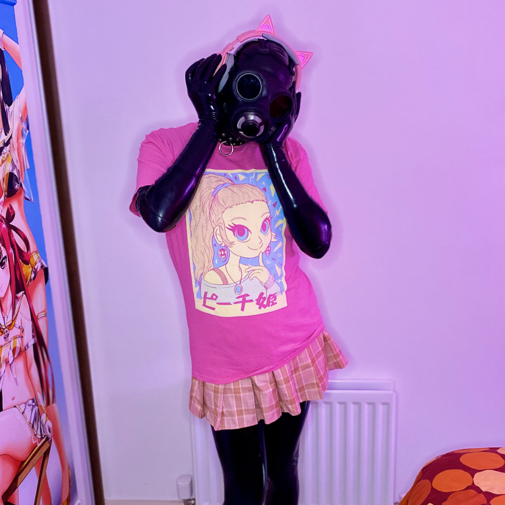 Rina wearing a black latex catsuit, black gas mask, toe shoes, pink t-shirt, and pink skirt, while holding pink cat-ear headphones on her head