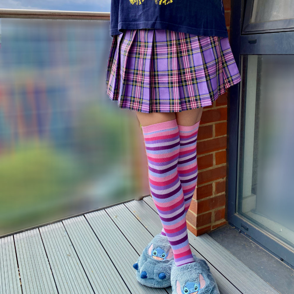 Rina is wearing a purple plaid skirt and purple-and-pink knee-high socks, leaving a sliver of bare thigh visible
