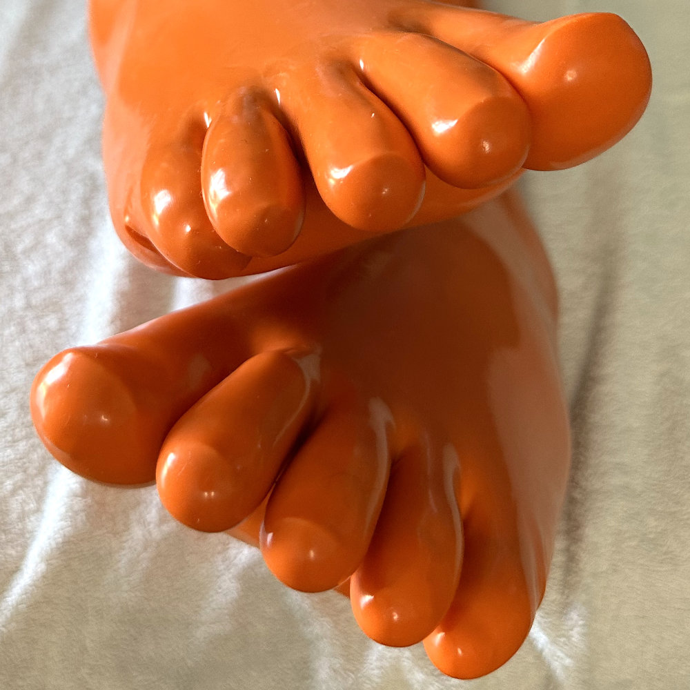 My feet and toes in shiny knee-high orange latex toe socks. The shot is composed with one foot over the other, with all ten toes visible