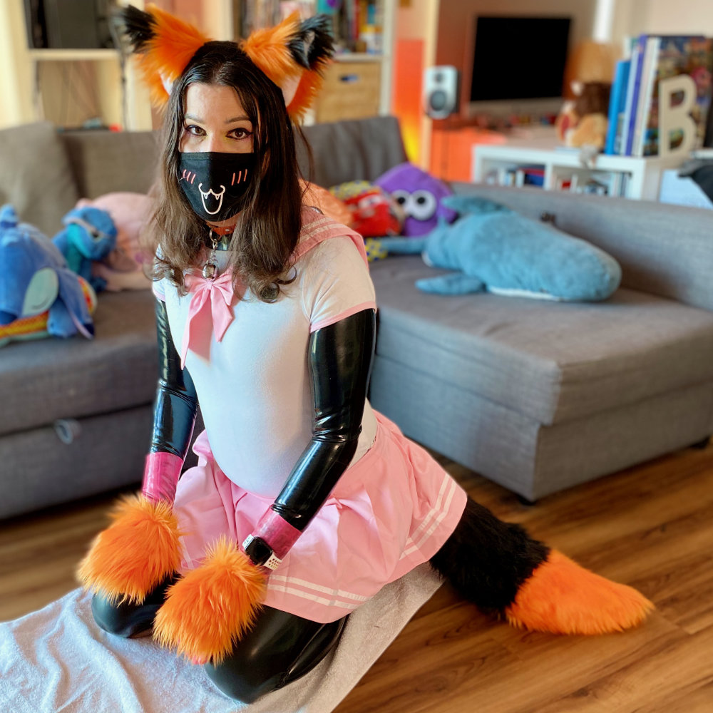 Rina kneeling on floor, wearing a black latex catsuit with pink latex gloves, a white and pink Japanese schoolgirl uniform, and black & orange fox ears, tail, and paws