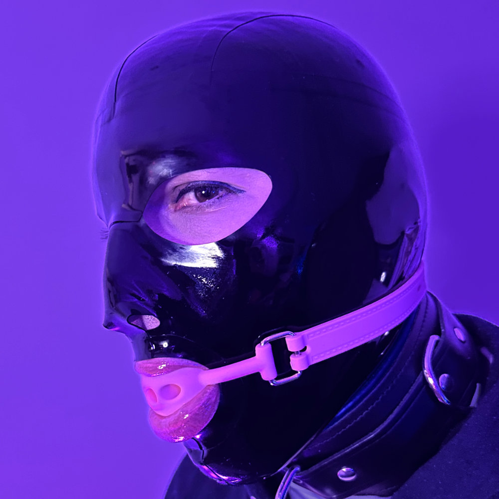 Rina wearing a shiny black latex hood with a pink ball gag forcing her mouth open. Her glossy pink lips are surrounding the ball and light is reflected in black shiny latex and her glossy lips.